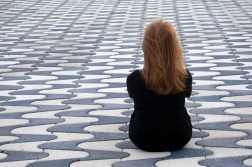 Girl sitting on colorful flagstones. She turned her back which causes a feeling of loneliness.